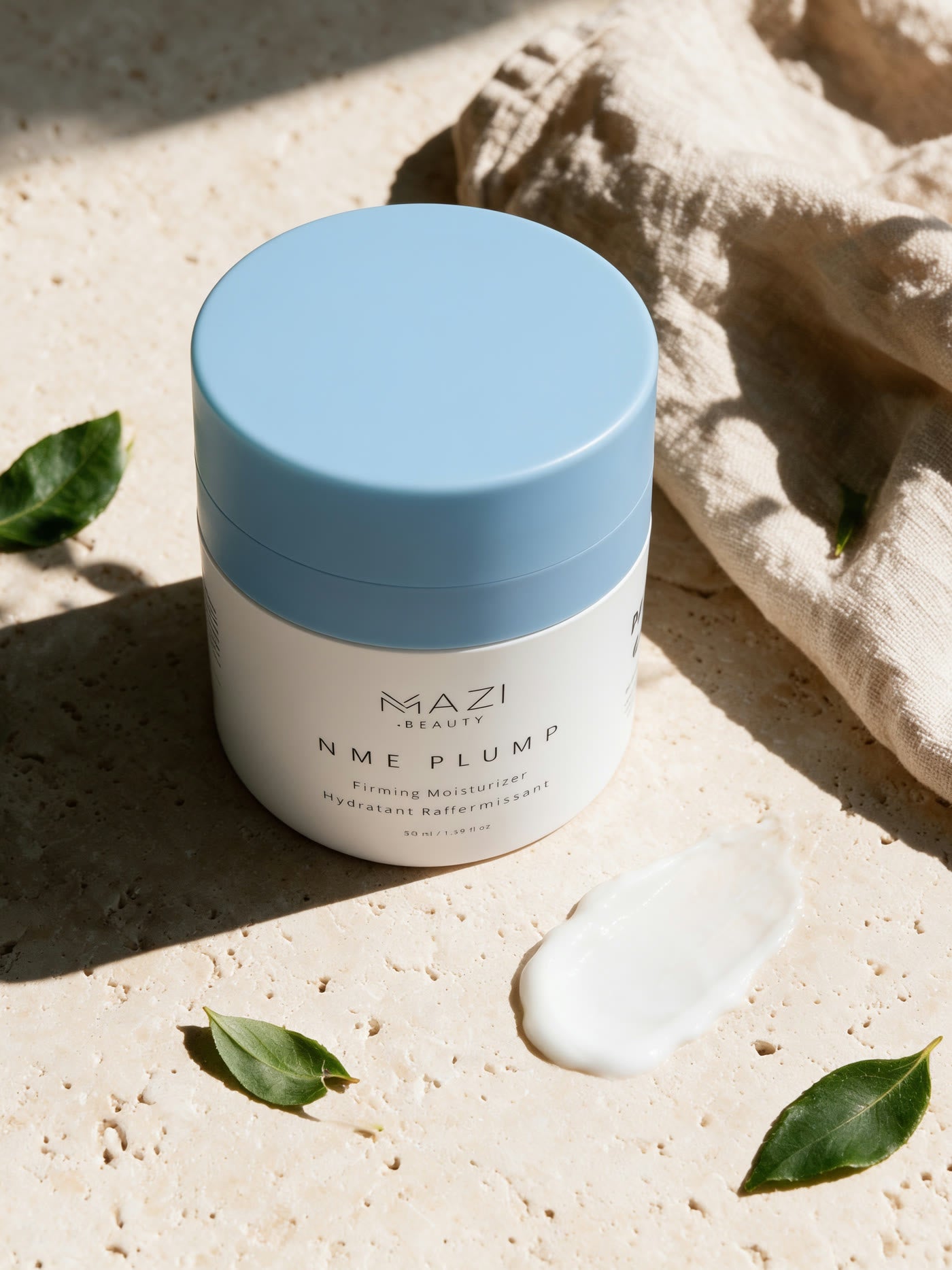 Le pot fermé de crème NME Plump sur du travertin à côté d'un lin froissé, avec une touche de crème à côté