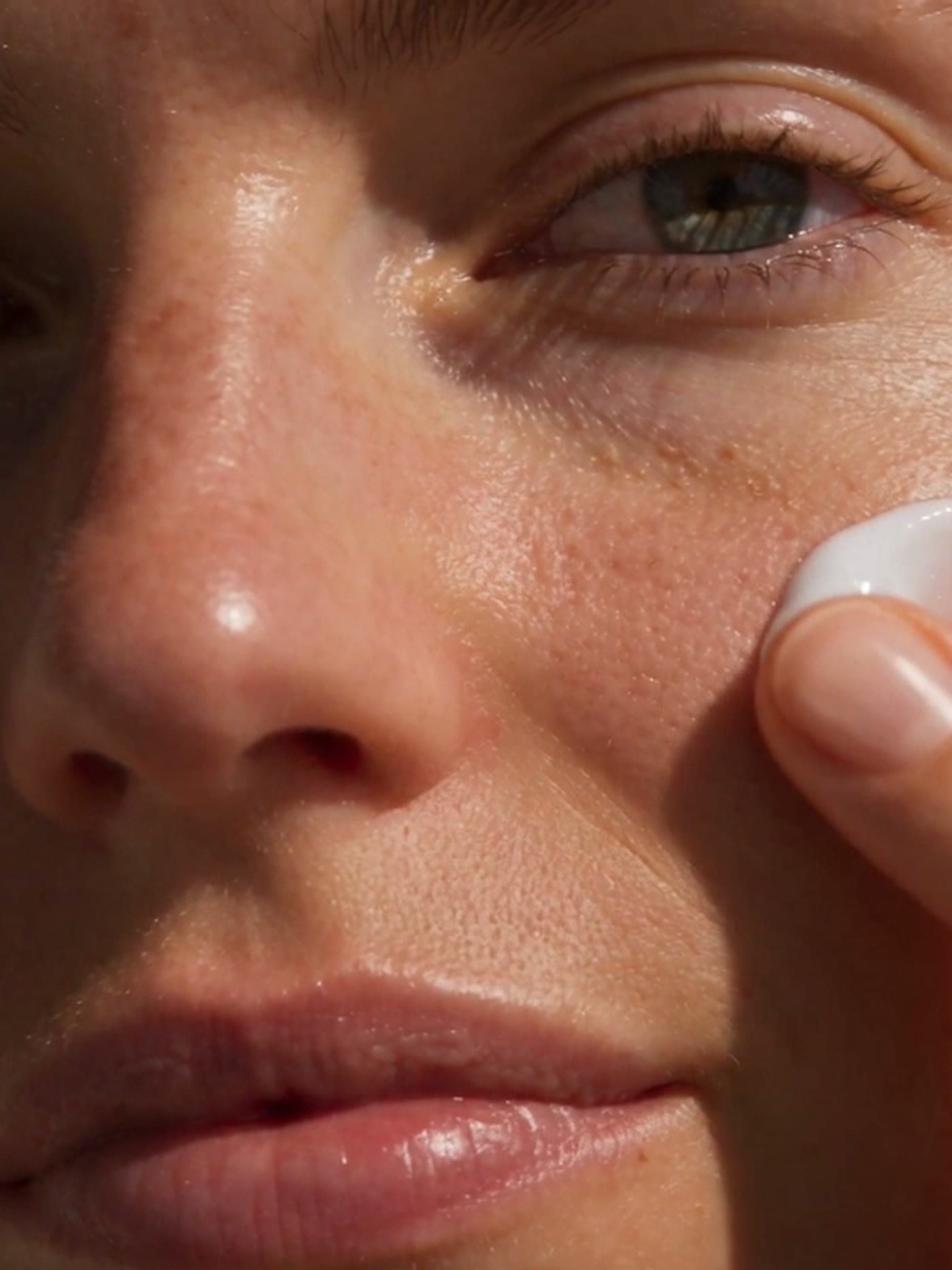 Une femme applique la crème blanche NME Plump sur sa joue du bout du doigt
