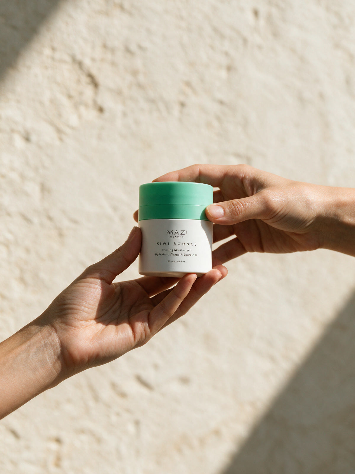 A hand holds the closed Kiwi Bounce day cream jar in front of a travertine wall