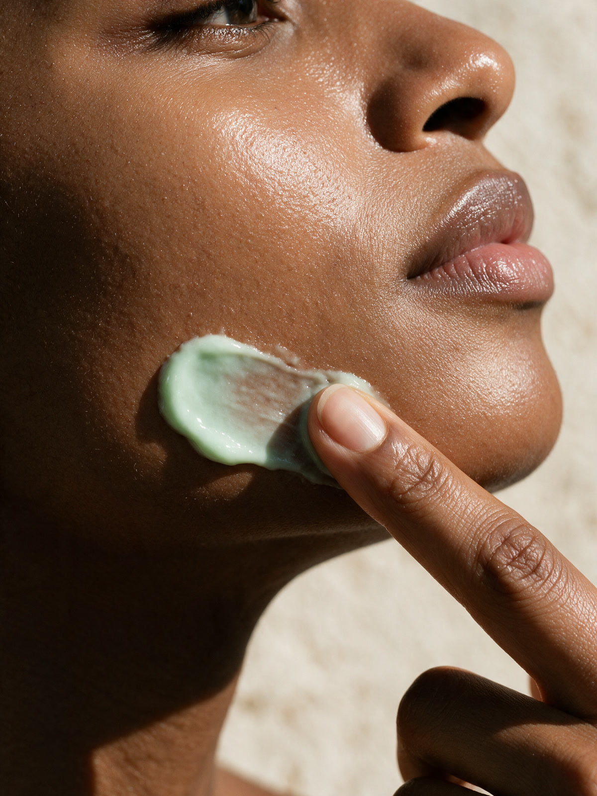 A woman spreads the pale green Kiwi Bounce day cream along her jawline in the sun