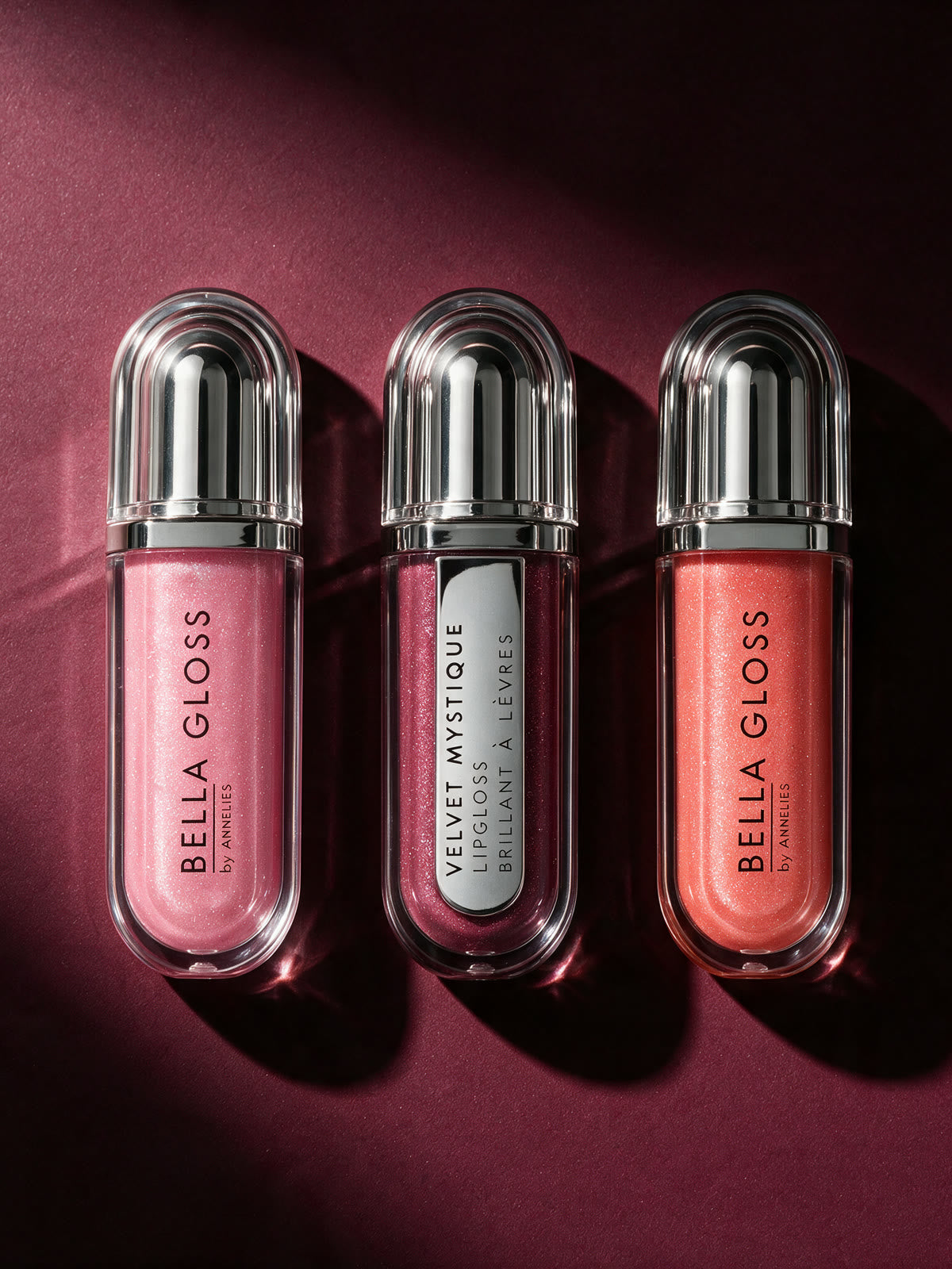 Les trois teintes du Bella Gloss Set vues d’en haut, côte à côte sur un fond rouge profond