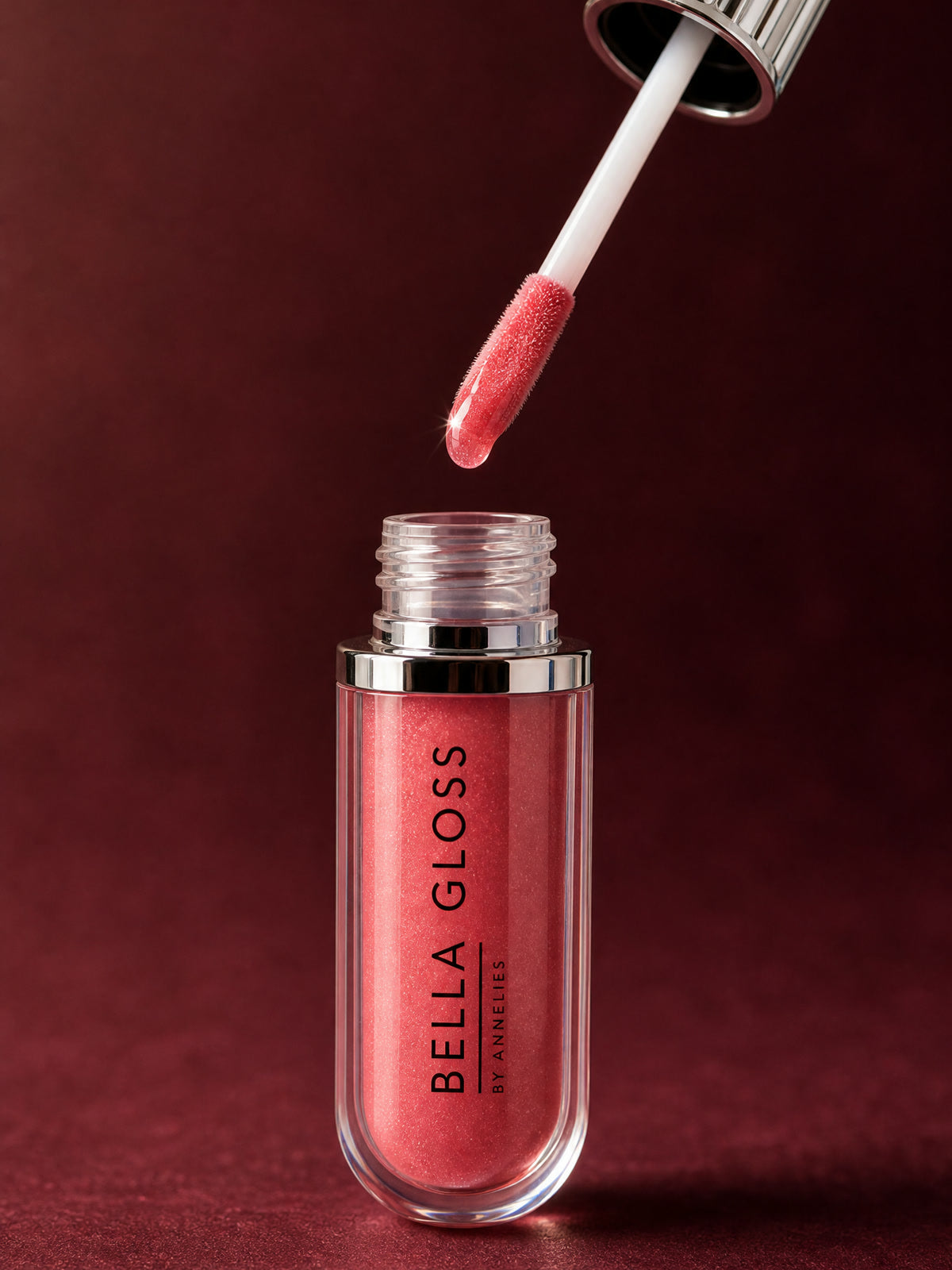 L’applicateur du gloss à lèvres Bella Gloss flotte au-dessus du tube ouvert, chargé de gloss