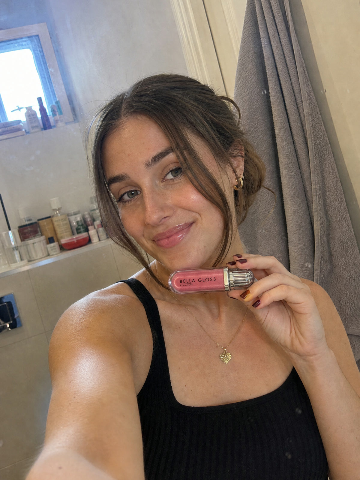 Une jeune femme tient le gloss à lèvres Bella Gloss dans sa salle de bains