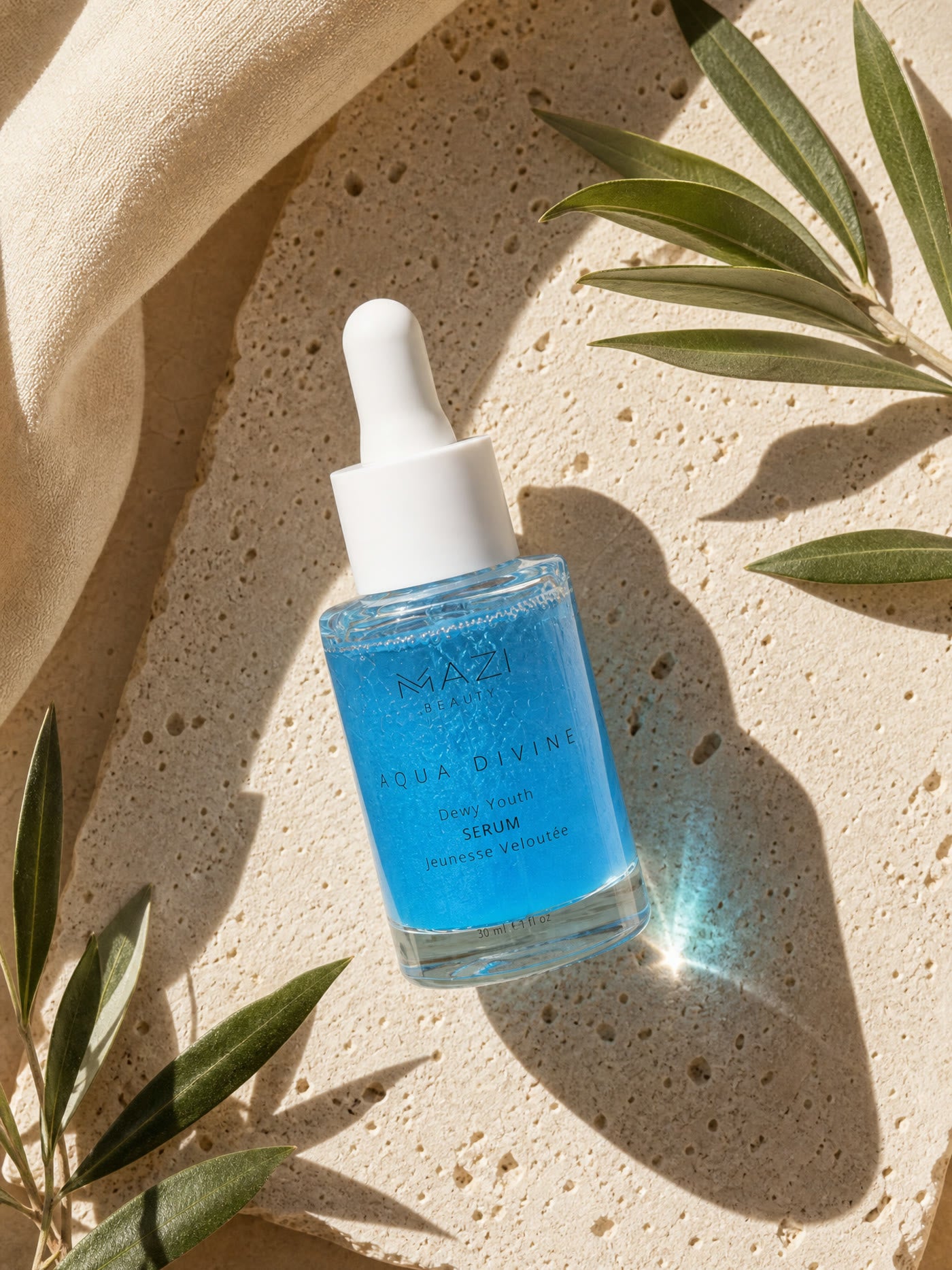The closed Aqua Divine serum bottle on travertine, olive leaves casting sharp shadows around it
