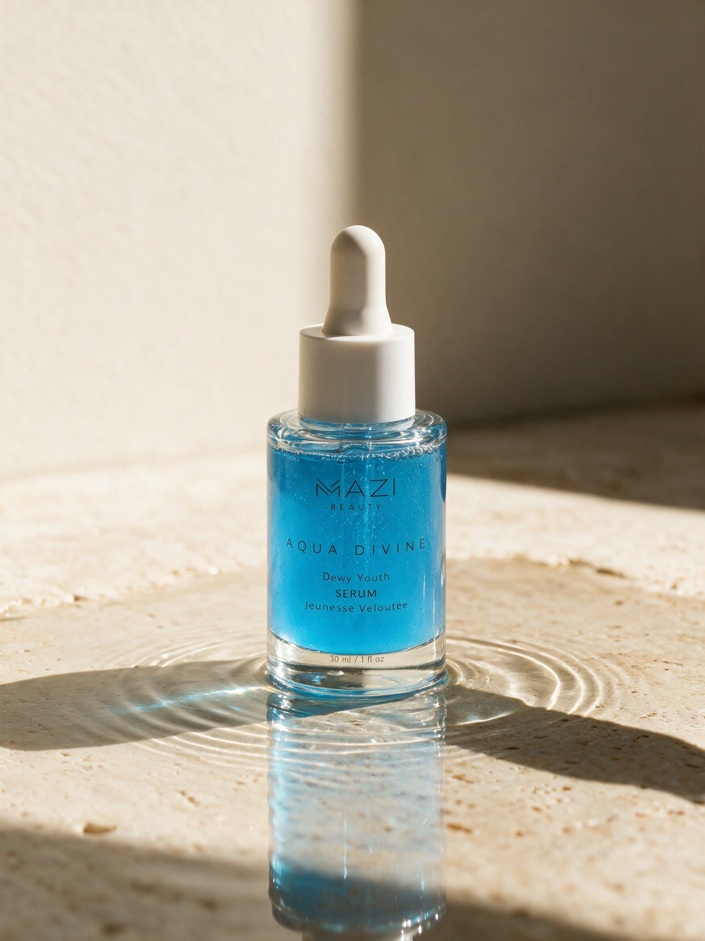 The closed Aqua Divine serum bottle standing in a still pool of water, a ripple spreading around it