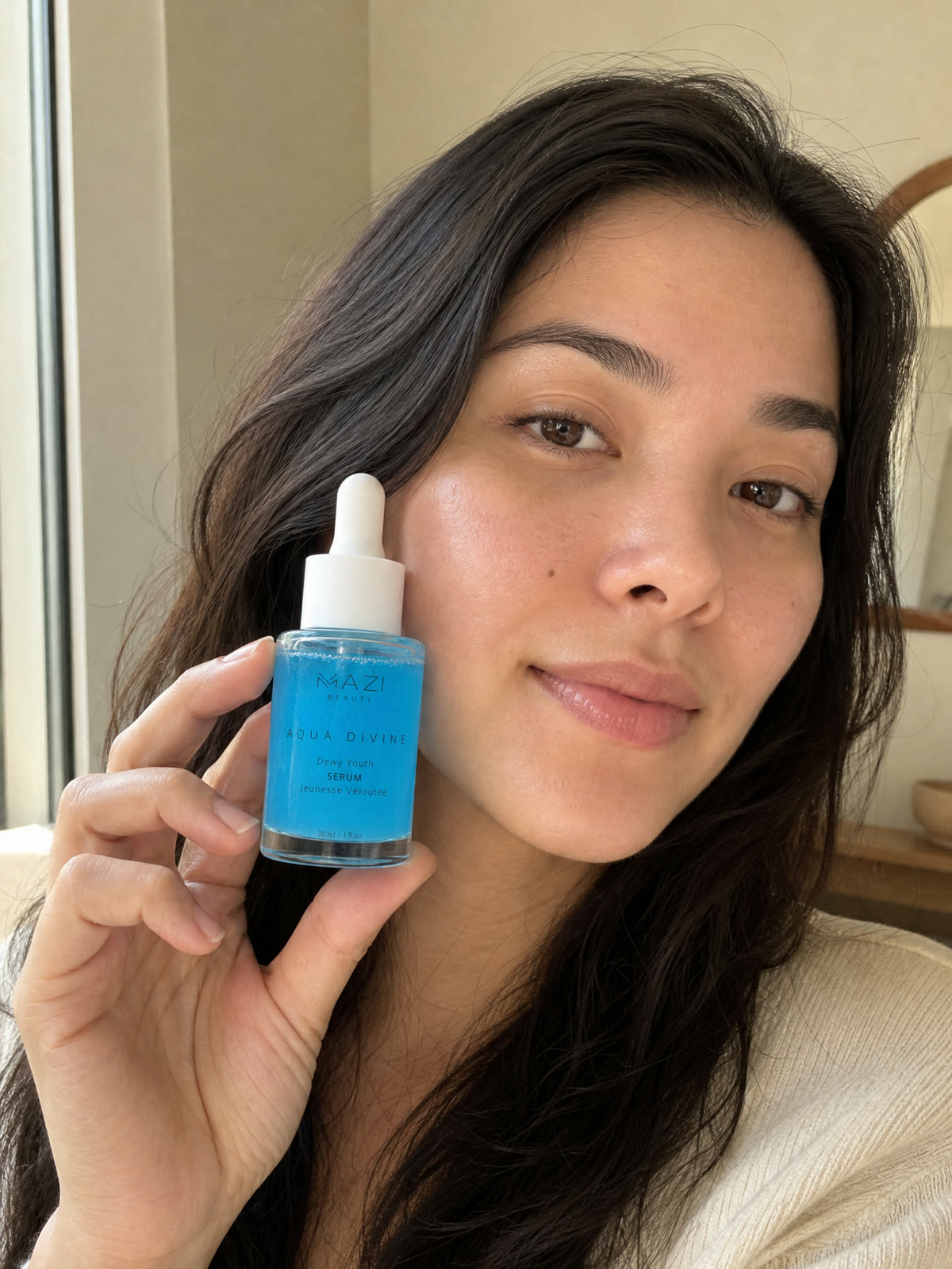 A woman holds the Aqua Divine serum bottle up beside her face in daylight