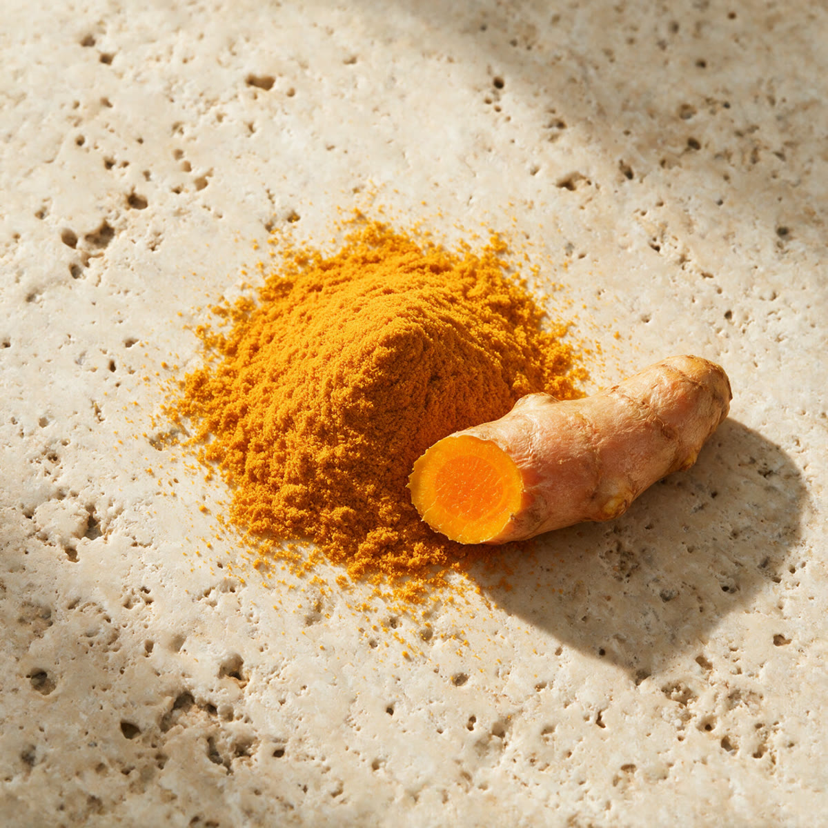 Ground turmeric and a piece of root on travertine in hard daylight