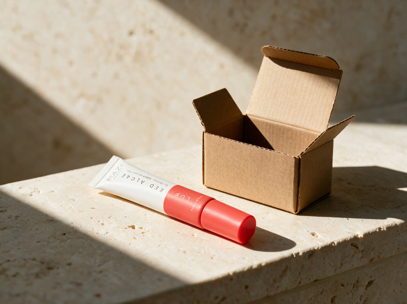 The closed LUR Red Algae tube on travertine beside a plain unmarked cardboard shipping box