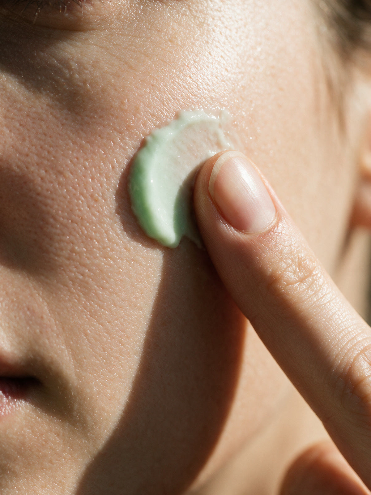A fingertip carrying a dot of pale green Kiwi Bounce day cream touches the cheek