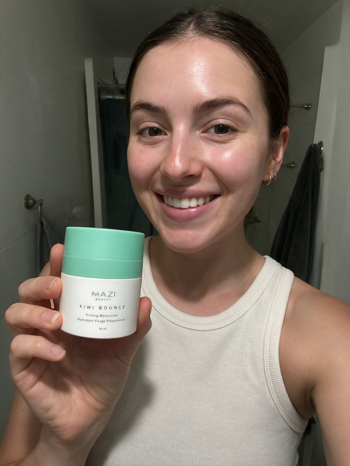 A woman in a white vest holds the Kiwi Bounce day cream jar up to the camera in her bathroom