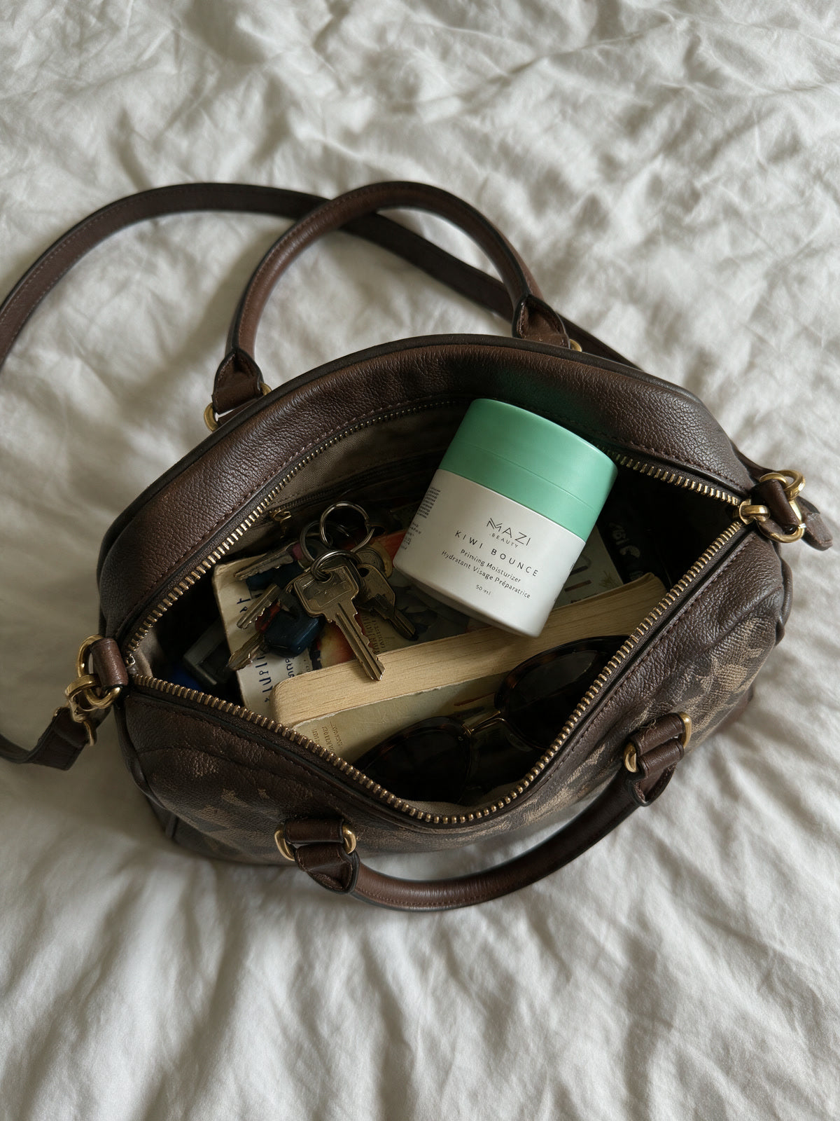 The Kiwi Bounce day cream jar sits in an open leather handbag on a bed